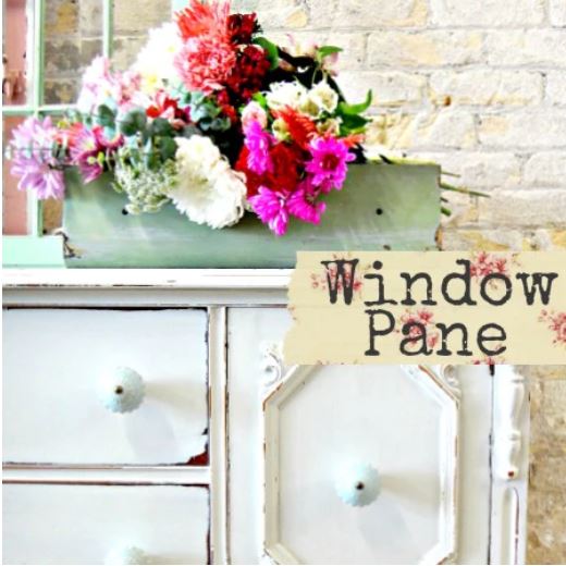 Floral arrangement in a green container on a white cabinet with 'Window Pane' sign.