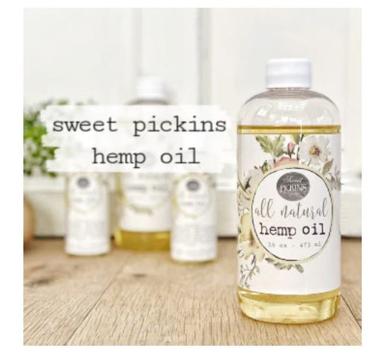 Bottle of Sweet Pickins hemp oil with a floral label on a wooden surface.