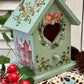 Decorative birdhouse with floral designs and a heart-shaped opening on a textured surface.