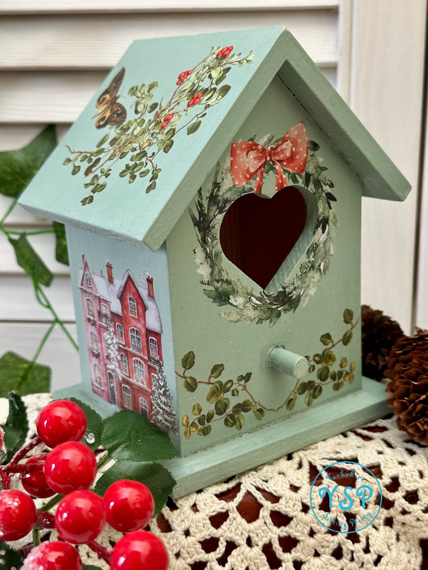 Decorative birdhouse with floral designs and a heart-shaped opening on a textured surface.