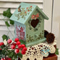 Decorative birdhouse with floral patterns on a wooden surface with red berries and greenery.
