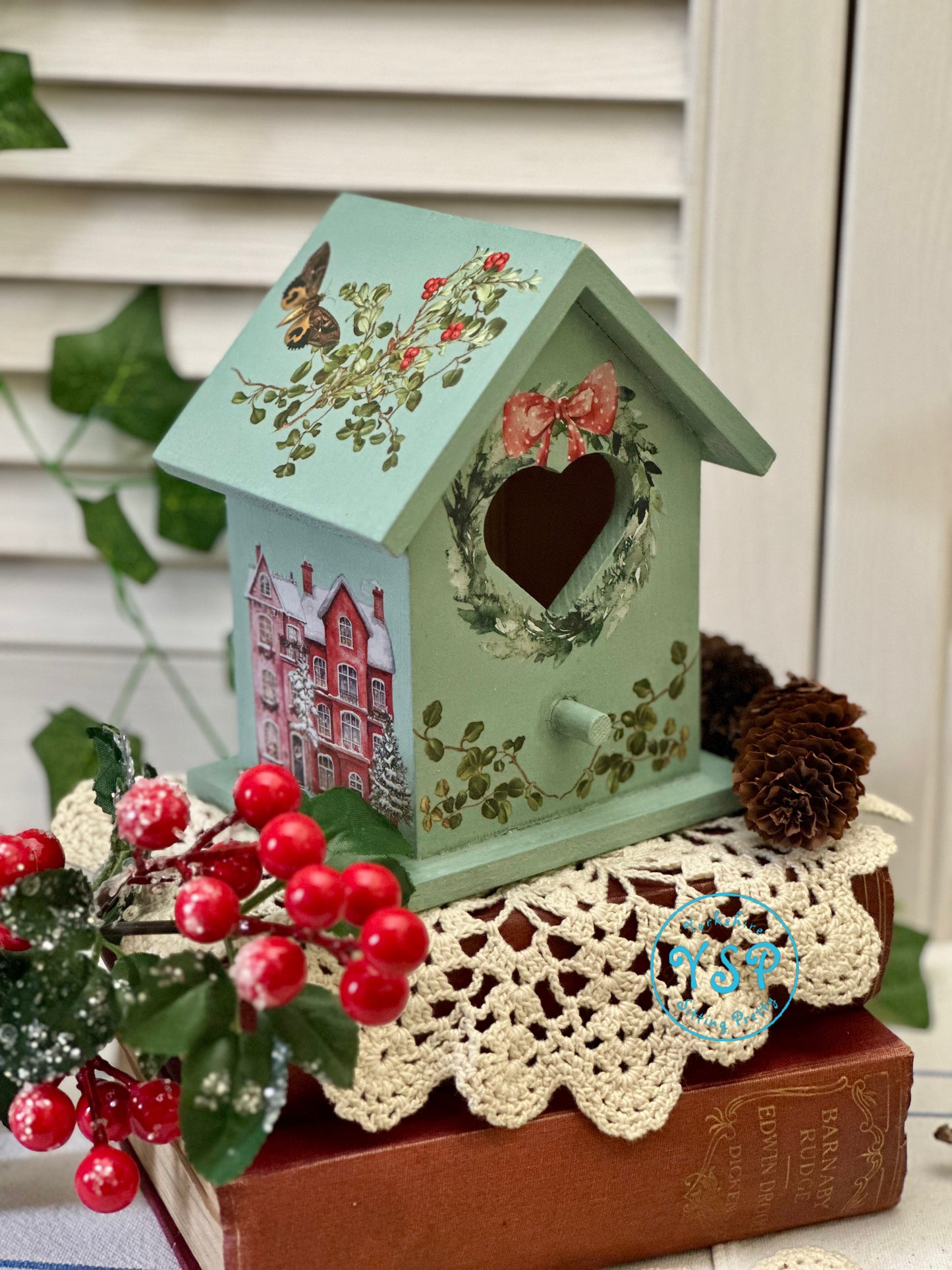 Decorative birdhouse with floral patterns on a wooden surface with red berries and greenery.