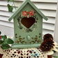 Decorative green birdhouse with a heart opening standing on a crotchet doily