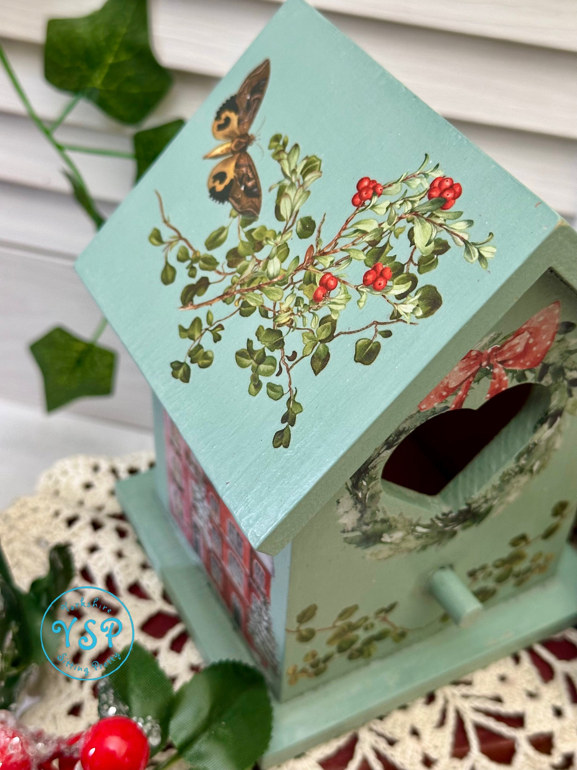 Decorative birdhouse with floral design and butterfly on a textured surface