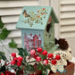 Decorative birdhouse with floral design on a stand with red berries and greenery.