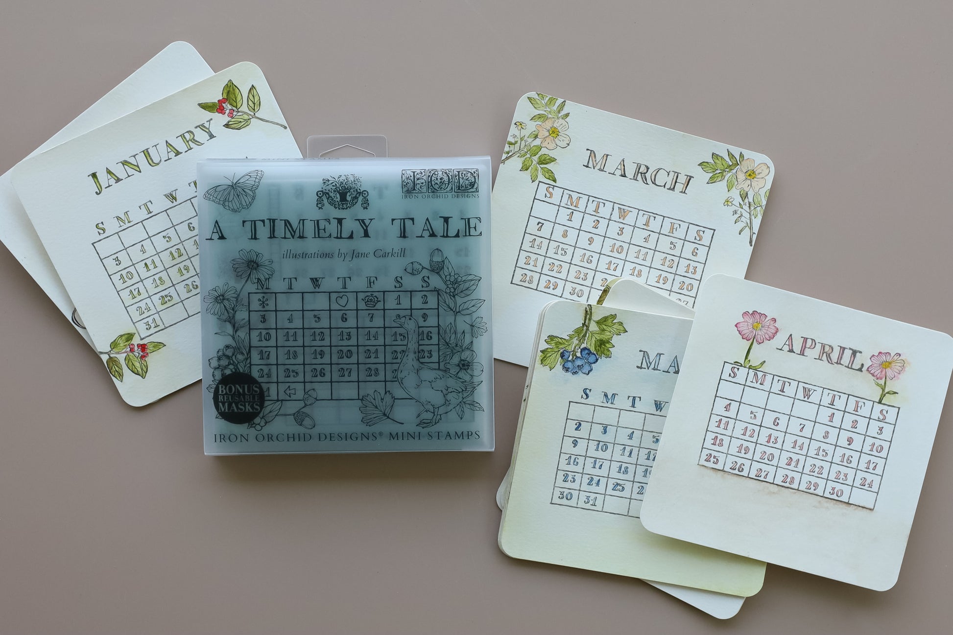 A set of monthly calendar cards with vintage floral designs and a central clear plastic box containing a stamp labeled 'A TIMELY TALE', arranged on a solid taupe background. A Timely Tale Stamp from Iron Orchid Designs.