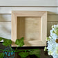 Wooden picture frame on a wooden surface with greenery and flowers by Iron Orchid Designs