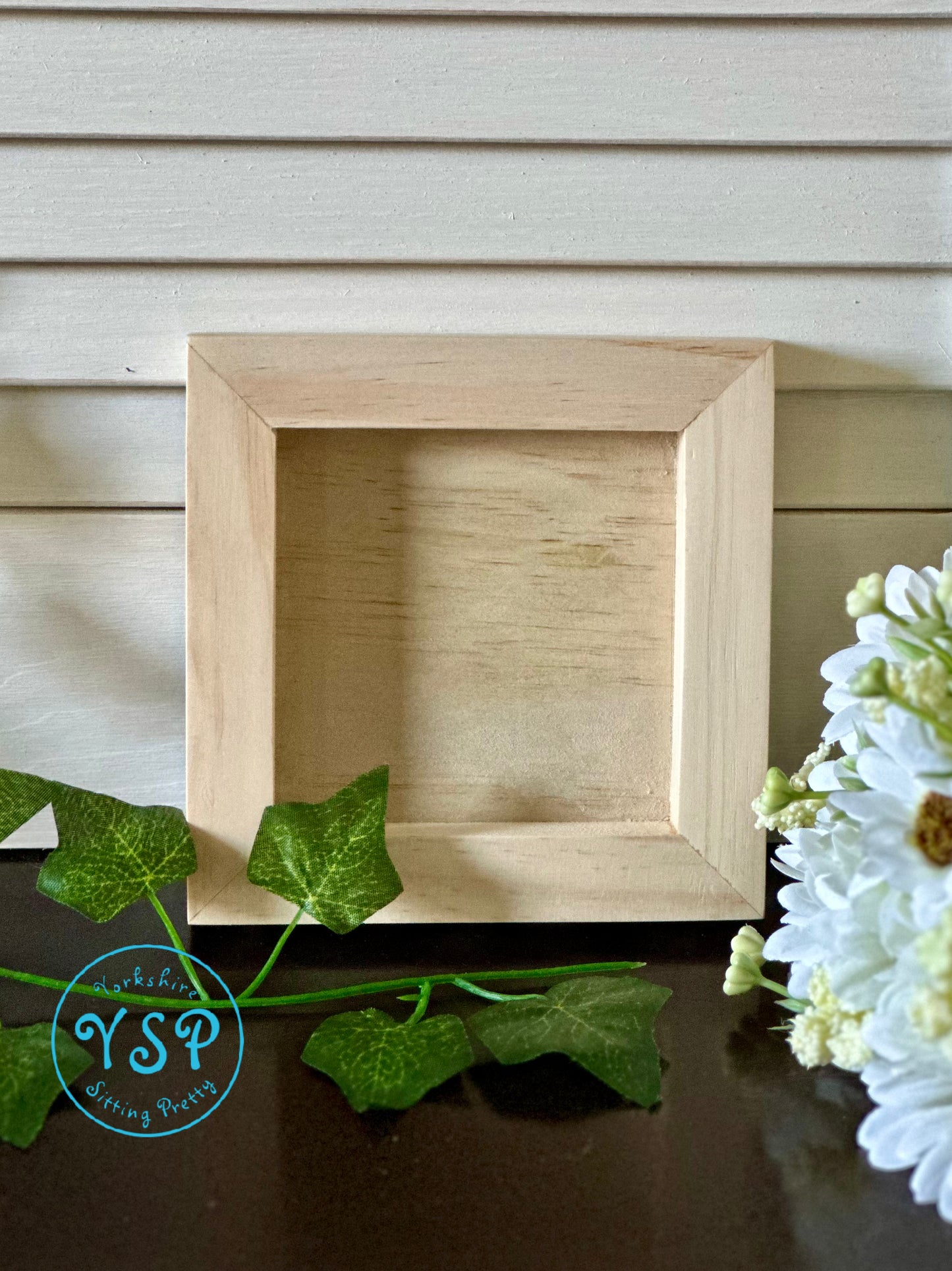 Wooden picture frame on a wooden surface with greenery and flowers by Iron Orchid Designs