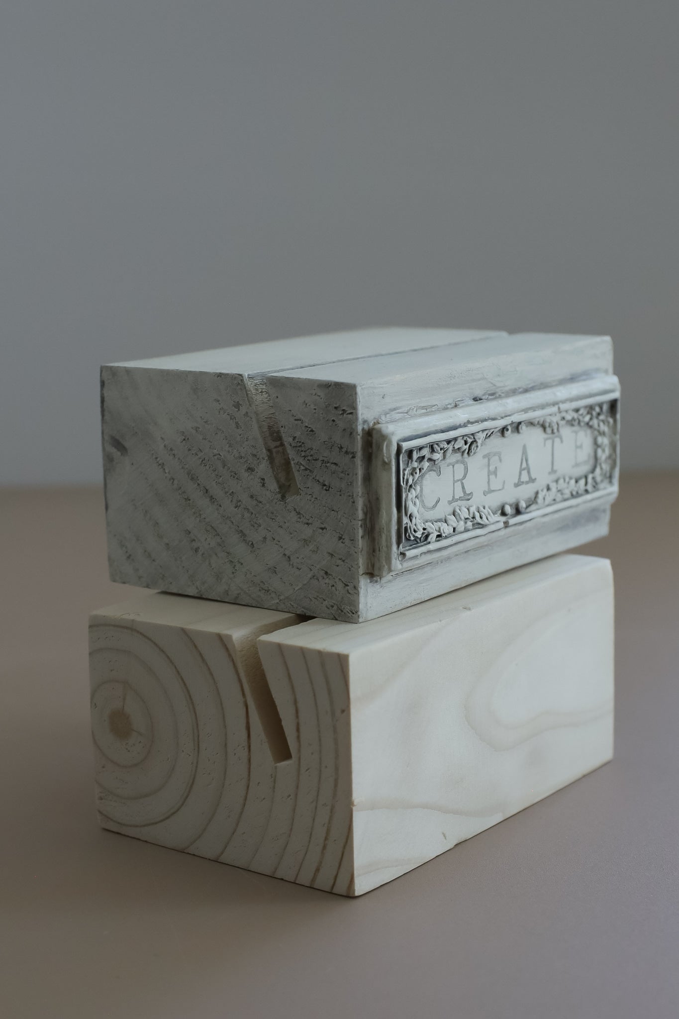 A small decorative wood stand with a distressed white painted top and a carved wood base, photographed against a plain gray background. From Iron Orchid Designs.