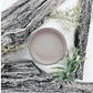 Pot of grey paint next to driftwood and moss. Paint Couture