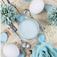 Pot of pale blue paint next to blue flowers. Paint Couture