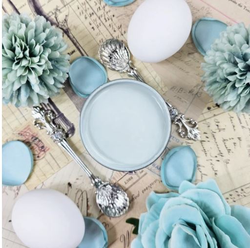 Pot of pale blue paint next to blue flowers. Paint Couture