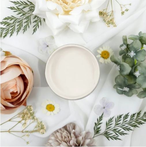 Pot of pale coloured cream paint on a white tablecloth surrounded by leaves and flowers. Paint Couture