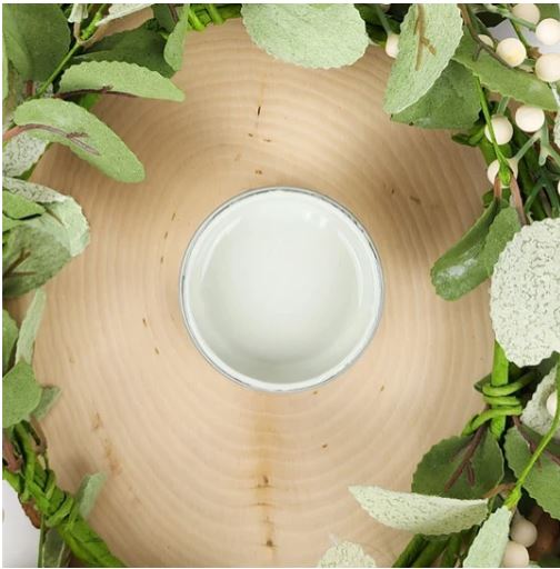 A small round container filled with pale green paint, centered on a light wood slice and surrounded by green foliage and white berries. Paint Couture