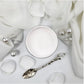 A pot of white paint, styled on a white fabric background with a silver spoon, pearl-like beads, and soft draped cloth. Paint Couture