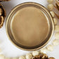 A round pot of Bronze Lux Metallic from Paint Couture, styled with white pearl beads and gold pinecones on a white background.