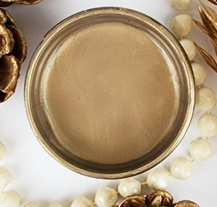 A round pot of Bronze Lux Metallic from Paint Couture, styled with white pearl beads and gold pinecones on a white background.
