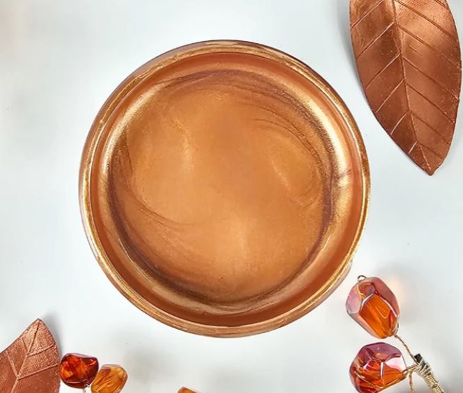 A round pot filled with Copper Lux Metallic by Paint Couture, shown from a top-down view on a white background with decorative copper leaf and amber bead props.