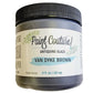 A jar of Paint Couture Antiquing Glaze in Van Dyke Brown, featuring a white label with green botanical illustrations and a black ribbed lid, set against a plain white background.