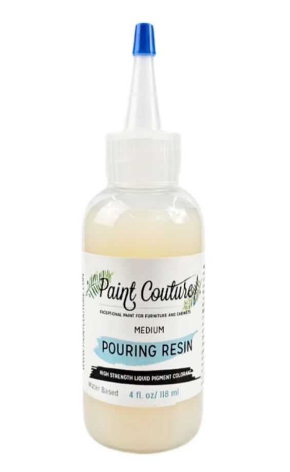 A bottle of Paint Couture Medium Pouring Resin with a white cap, clear plastic body showing the pale cream-colored resin inside, and a blue-tipped applicator nozzle.