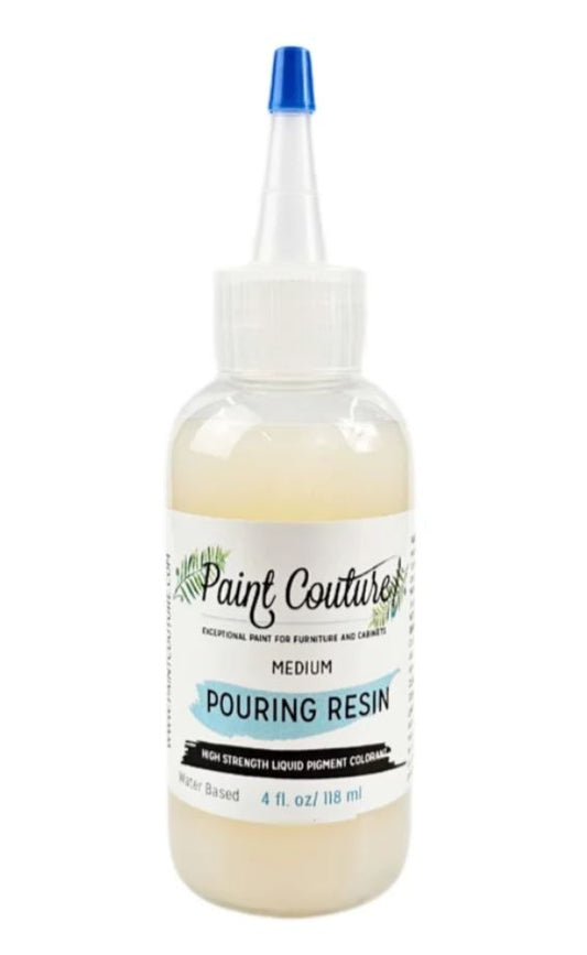 A bottle of Paint Couture Medium Pouring Resin with a white cap, clear plastic body showing the pale cream-colored resin inside, and a blue-tipped applicator nozzle.