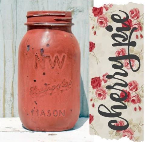 Red mason jar with 'NW Mason' branding next to a decorative sign with 'cherry pie' text and floral design.
