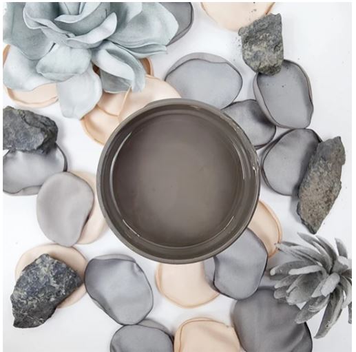 A round pot of dark taupe-brown colour paint surrounded by decorative faux succulents and smooth gray and beige stones on a white background. Paint Couture