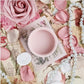 A small pot of pink paint surrounded by pink roses, petals and pearl beads. Paint Couture