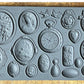 Iron Orchid Designs Cameos Mould. Grey mould laying on a wooden surface. Beautiful intricate designs of cameos, hearts and flowers.