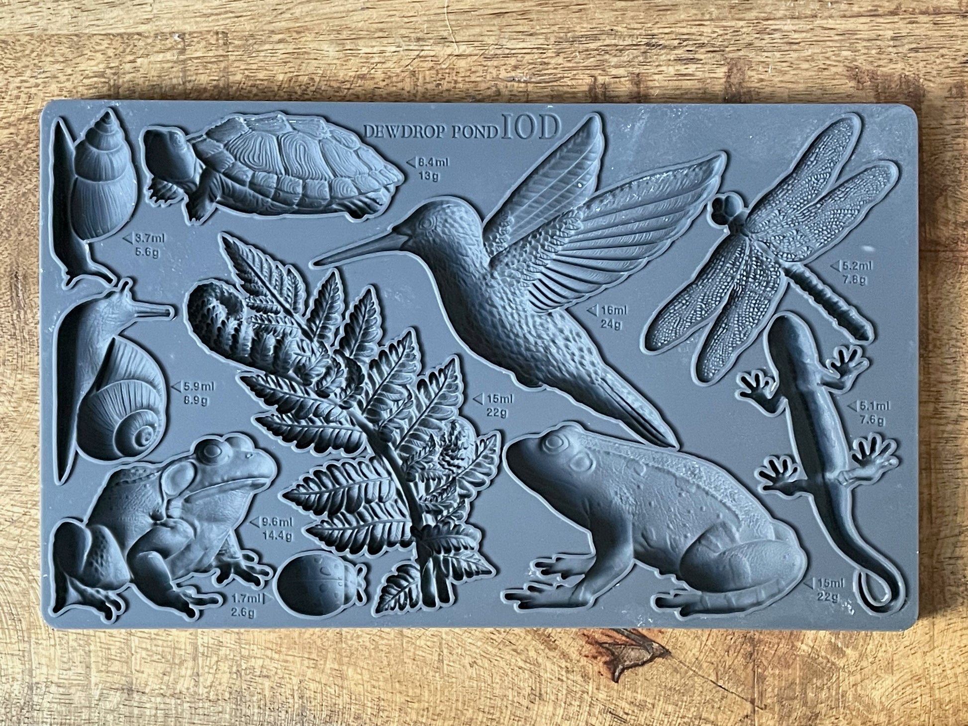 Iron Orchid Designs Dewdrop Pond grey Mould laying on a wooden surface. Highly detailed hummingbird, dragonfly, fern, frog, tortoise designs.