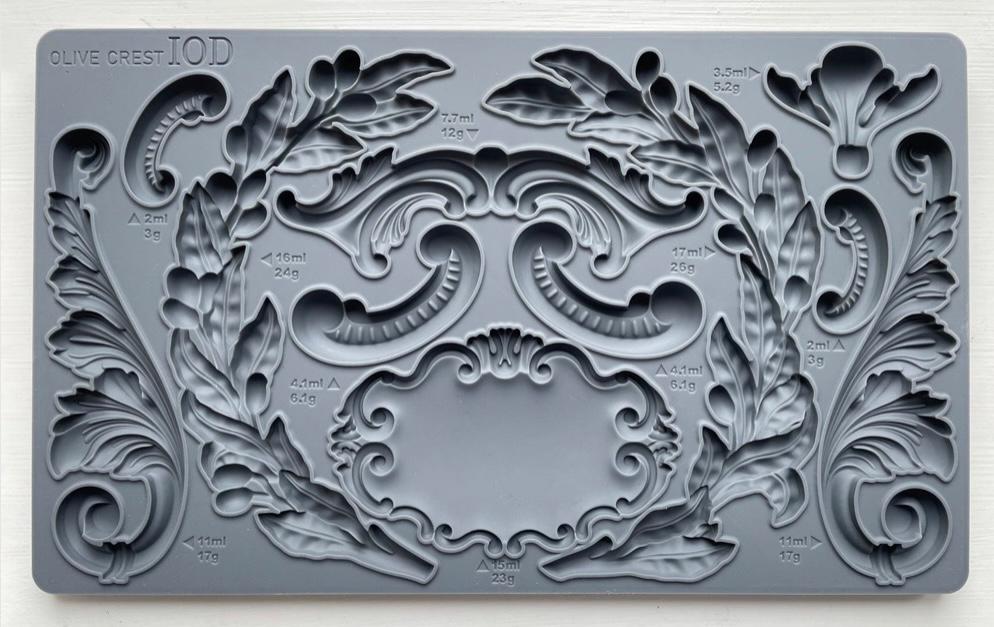 Iron Orchid Designs Olive Crest grey silicone mould on a white background. There are intricate designs of olive branches, swags, curls and a decorative label