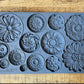 Iron Orchid Designs Rosettes grey silicone Mould laying on a wooden surface. There are twelve designs.