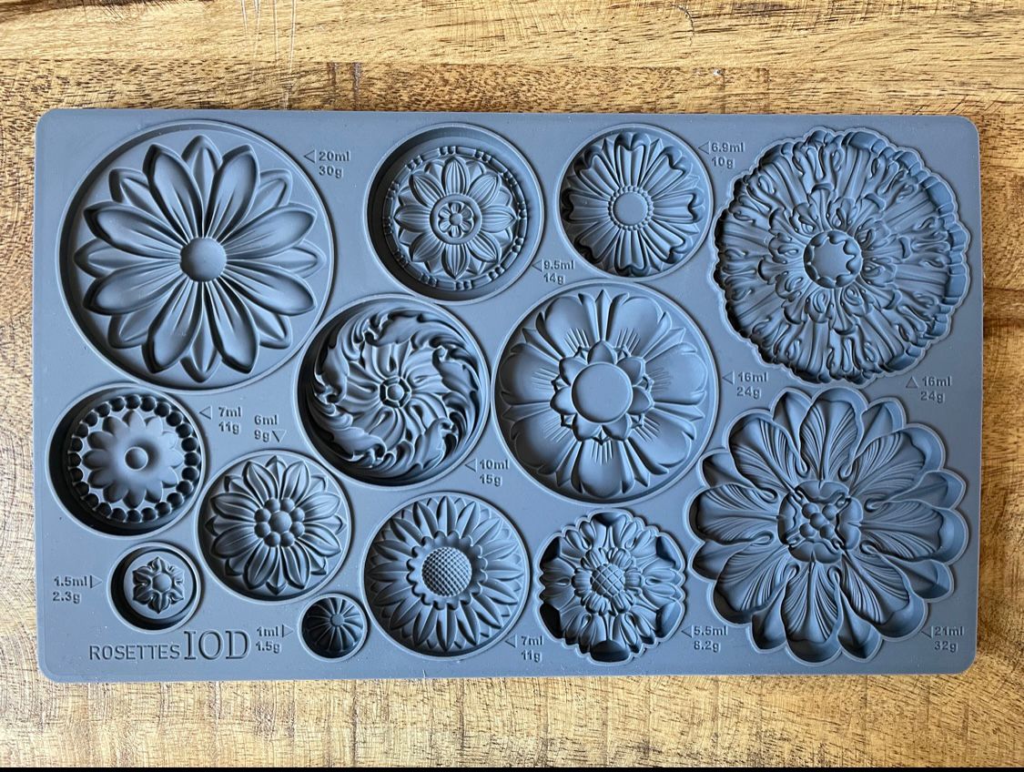 Iron Orchid Designs Rosettes grey silicone Mould laying on a wooden surface. There are twelve designs.