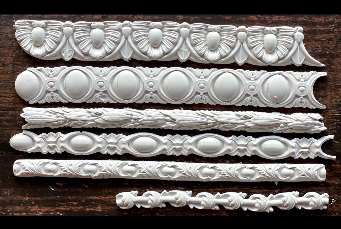 White clay castings from Iron Orchid Designs Trimmings Three decorative trims Mould laying on a wooden surface